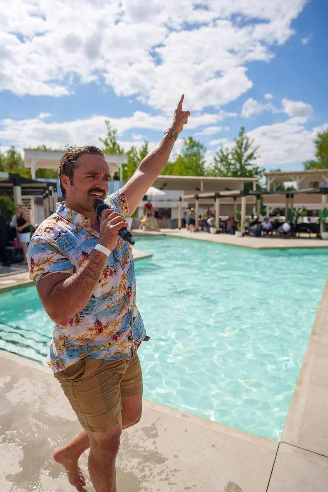 Dominic, trempé, le bras levé au bord de la piscine